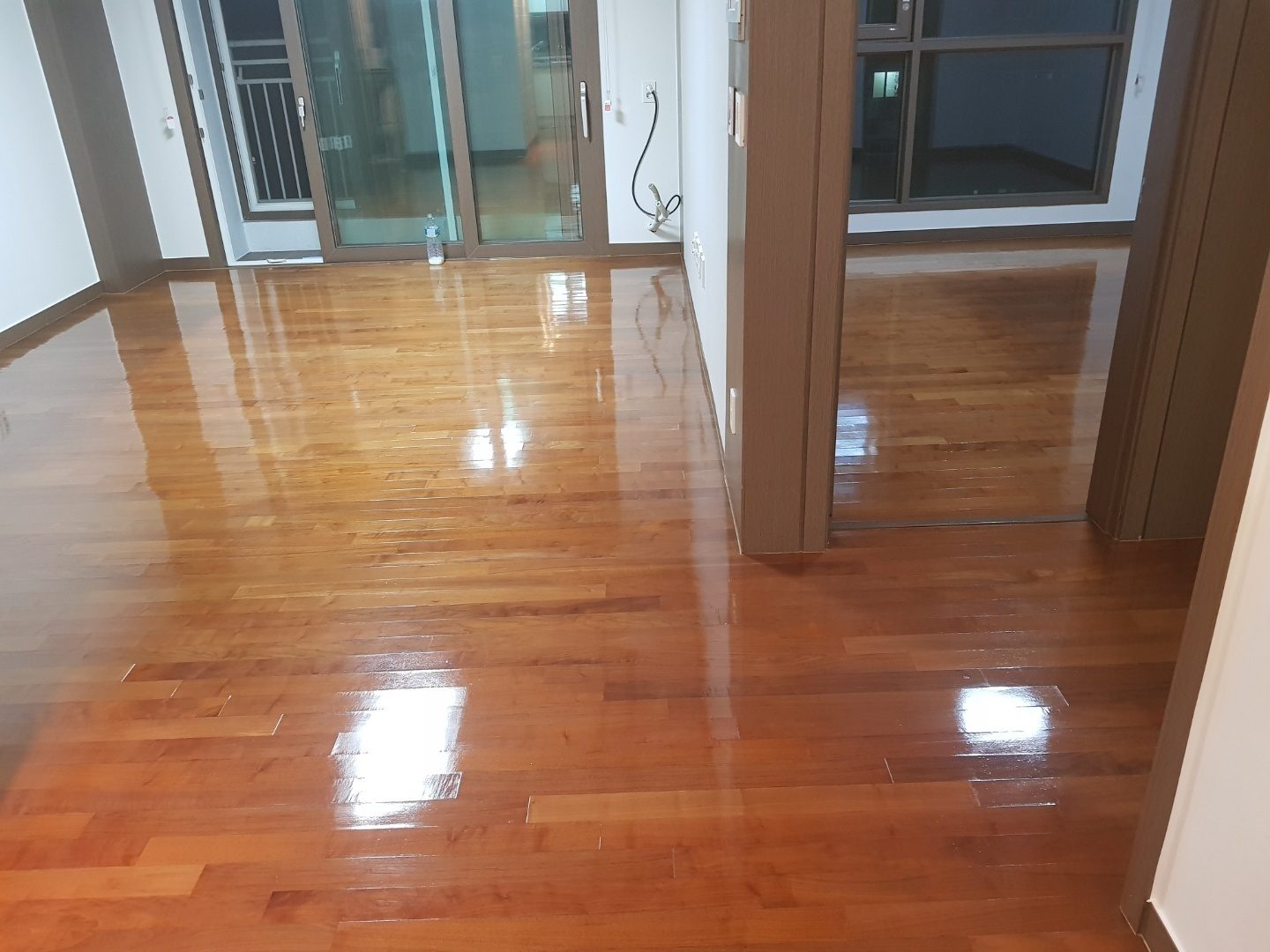 아파트 거실에 깔린 짙은 색 강마루 — 통로까지 이어지는 결